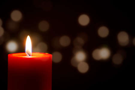 Red Candle with fire against defocused lights in darkness with golden bokeh in the dark Backgroundの写真素材