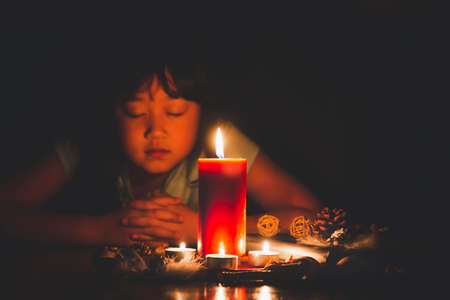 Woman Praying and worship to GOD Using hands to pray in religious beliefs and worship christian with Red Candle with fire against defocused lights in darkness with in the dark Backgroundの写真素材