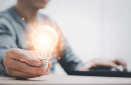 businessman hand holding light bulb and working with computer on the desk, saving energy and money,The idea of ââinspiration from online technology.innovation idea, Intellectual imagination concept.の写真素材