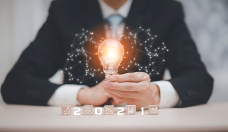 Businessman hand holding light bulb with icon on wood cube and   working on desk, Creativity and...
