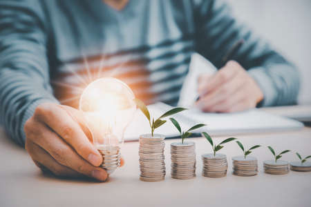 thinking and creative concept, businessman hand holding light bulb with coins stacking on desk.saving energy and money,The idea of ââinspiration from online technology.innovation idea concept.の写真素材
