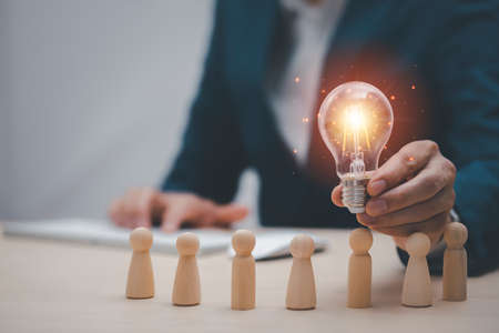 thinking and creative, Businessman hand holding light bulb on the wooden people, Teamwork and idea concept, Successful team leader, Businessman hand choose people standing out from the crowd.の写真素材