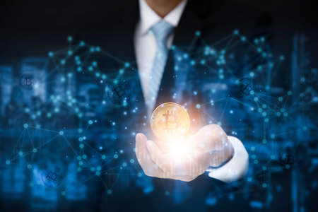 Businessman is holding a bitcoin as part of a business network on blue background. bitcoin cryptocurrency ideas concept and virtual financial chart diagram,Digital symbol of a new virtual currencyの写真素材