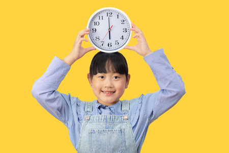 Time and daily life concept, Happy Asian little girl hand holding a big clock in the yellow...