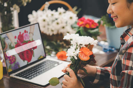 Online home flower arrangement concept, asian woman Smiling florist record video broadcast or course on smartphone or computer, compose arrange floral decorations,online flower shopの写真素材