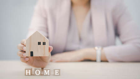 Woman hand holding mini wood house model and wood cubes of business from model on wood table, Planning buy Real Estate, Planning to buy property. Home insurance and security ideas concept.の写真素材