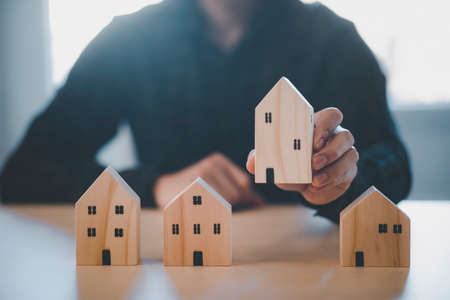 Man hand choosing mini wood house model from model on wood table, Planning buy Real Estate, Planning to buy property. concept of Choose the best.の写真素材