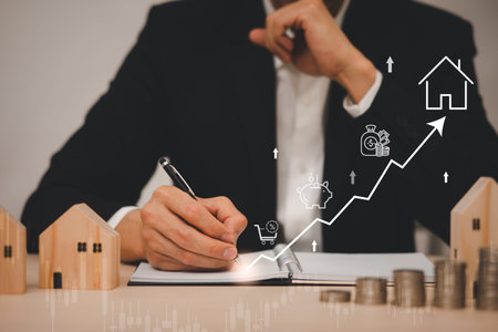 Businessman hand write in book note and icon business graphs with mini wood house model from model on wood table, Planning buy Real Estate, Planning to buy property. concept of Choose the best.の写真素材