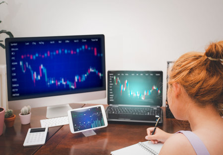 Asian young woman interacting with laptops, phones, and tablets with featuring stock tickers or...