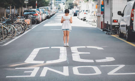 Asian Child is watching the phone on the road crossing or using a mobile phone for a long time hurts her eyes and has an aggressive atmosphere. Concept danger for children's mobile phones.の写真素材