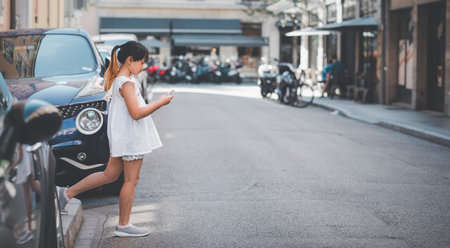 Asian Child is watching the phone on the road crossing or using a mobile phone for a long time hurts her eyes and has an aggressive atmosphere. Concept danger for children's mobile phones.の写真素材