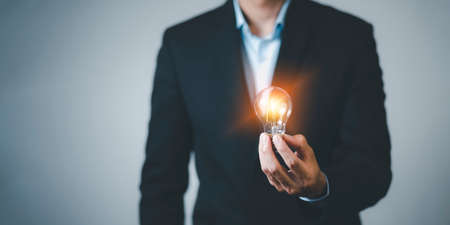 Businessman hand holding light bulb with line connect and working on the desk, Creativity and innovation are keys to success.Concept of new idea and innovation with energy and power , working at home,の写真素材