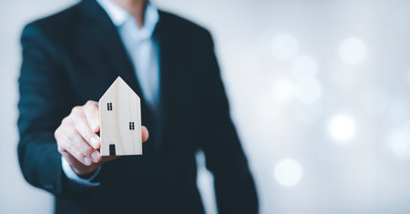 Businessman hand holding mini wood house model from the model on wood table, Planning buy Real Estate, Planning to buy the property. concept security of Choose the best.の写真素材
