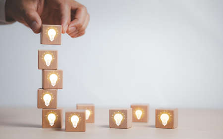 Wooden cube block tower with light bulb icon on white background, Conceptual of creative idea and innovation, New business idea, Creative and new idea, brainstorming creative idea and innovation.の写真素材