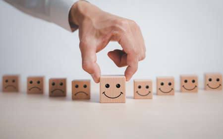 Customer service evaluation and satisfaction survey service rating concepts.Hand choose wooden cube block with icon face smile, Close up customer hand choose the happy face smile face icon on wooden.の写真素材