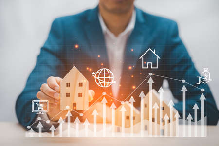 Man hand choosing mini wood house model from the model on wood table, Planning buy Real Estate, Planning to buy property. concept of Choose the best, Business market graph.の写真素材