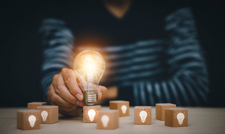 Man hand holding light bulb with Business icon on wood cube and working on desk, Creativity, and...