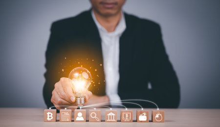 Man hand holding light bulb with Business icon on wood cube and working on desk, Creativity, and innovation are keys to success. Concept of new idea and innovation with Brain and light bulbs.の写真素材