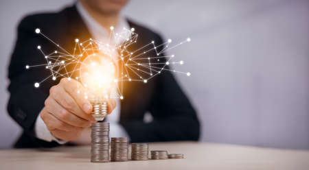 Businessman hand holding light bulb with line connect and Coins stack on the wooden table, Saving ideas and investment budget, Creative ideas concept of saving money  concept, Copy spaceの写真素材