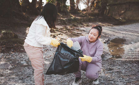Earth Day concept, Woman and daughter pick up garbage in litter bags, clean-ups in nature to recycling in their communities, clean river and protect environment from pollution, conservation Nature.の写真素材