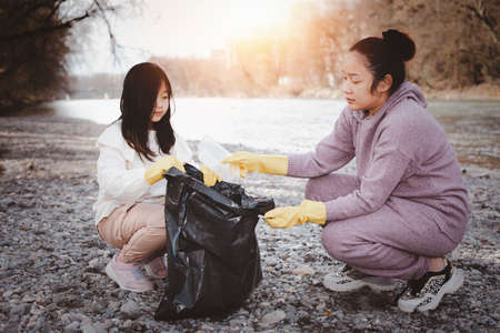 Earth Day concept, Woman and daughter pick up garbage in litter bags, clean-ups in nature to recycling in their communities, clean river and protect environment from pollution, conservation Nature.の写真素材
