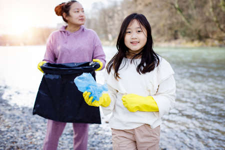 Earth Day concept, Woman and daughter pick up garbage in litter bags, clean-ups in nature to recycling in their communities, clean river and protect environment from pollution, conservation Nature.の写真素材