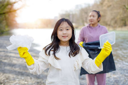 Earth Day concept, Woman and daughter pick up garbage in litter bags, clean-ups in nature to recycling in their communities, clean river and protect environment from pollution, conservation Nature.の写真素材