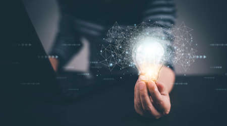 Businessman hand holding light bulb with icons and working on the desk, Creativity and innovation are keys to success.Concept of new idea and innovation with energy and power , working at home,の写真素材