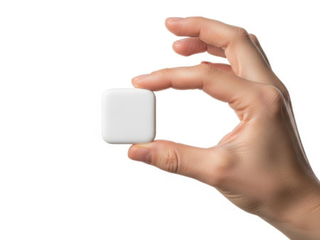 The image features a hand holding a small white cube against a white background. The cube is centered in the hand, creating a minimalist and clean composition. The hand is positioned in such a way that the fingers gently grasp the cube, emphasizing its small size and simplicity. The white background enhances the focus on the cube and the hand, making it a clear and visually appealing image.の素材