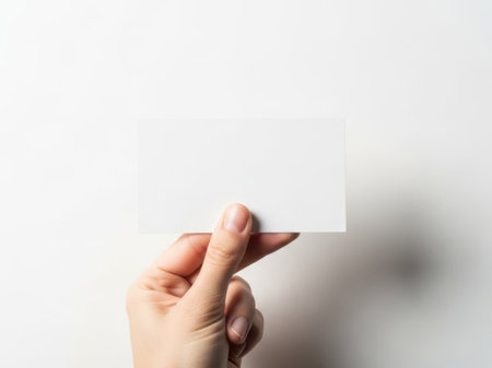 The image features a hand holding a white piece of paper against a white background. The simplicity of the image emphasizes the hand and the paper, making them the focal points. The white background provides a clean and minimalist aesthetic.の素材