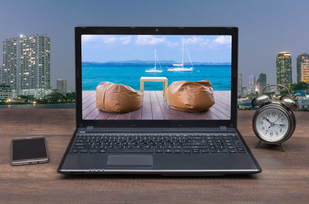 Front view of wooden office desktop with seating picture in moniter notebook, alarm clock, mobile on cityl background. Mock up.Concepcion wants to relaxの写真素材