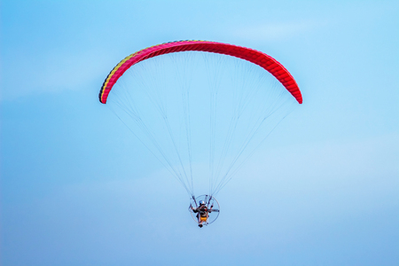 Rear view of man flying with paramotor glider parachute on beautiful blue skyの写真素材