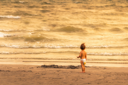 Baby in diapers are looking at the sea skeptically on the beach in the evening, the concept of learning.の写真素材