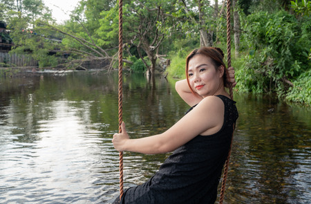 woman sitting on a swing along the stream Swing your feet through the water slowly and happily on a relaxing day.の写真素材