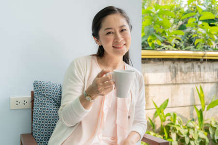 Middle-aged Asian women sit and sip coffee in the backyard.の写真素材