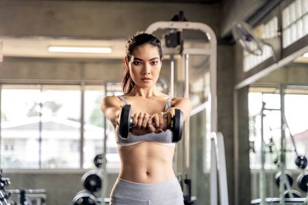 Asian beautiful woman is lifting double in the gym, She smile happily in exercise because it makes her shapely, the concept of exercise, lose weight, strengthen muscles.の写真素材