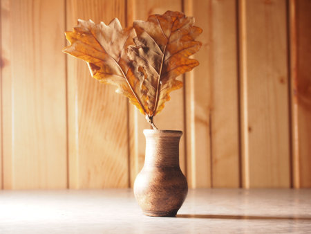 Autumn bouquet. Dry oak leaves in a vase of clay. The photo on the background of a wooden wall. Still-life.の写真素材