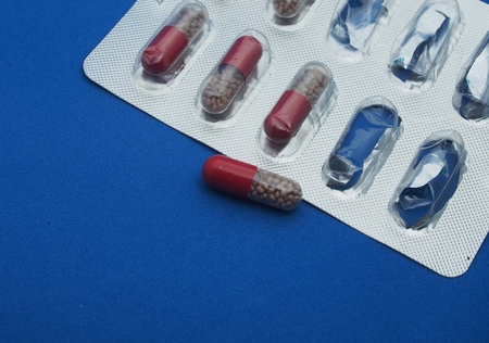 The drug in capsules. Capsules lie in plastic transparent packaging. Photo on a blue background. The capsules are brown granules.の写真素材