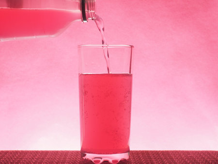 A pink carbonated drink is poured into a clear glass glass. Photo on a pink background. Still life