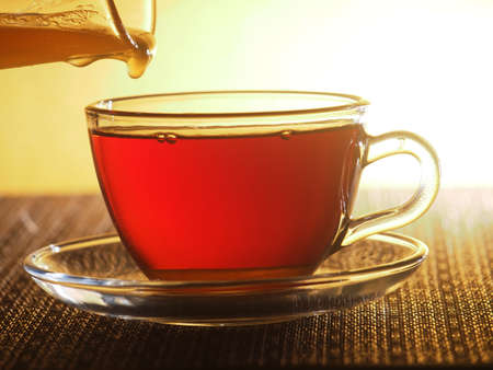 A glass Cup of tea is filled with honey from a glass container. Close up.の写真素材