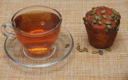 A cup of tea and a cupcake with pumpkin seeds are lying on a gray tablecloth. Still-lifeの写真素材