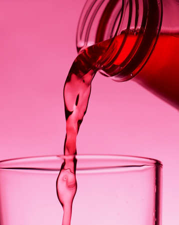A red drink is poured into a transparent glass from a bottle. Close-up.の写真素材