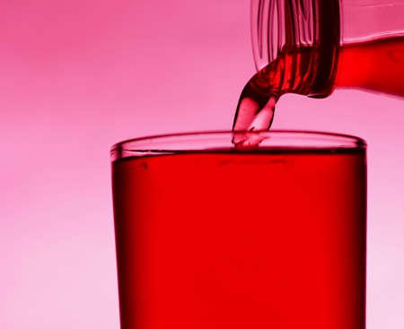 A red drink is poured into a transparent glass from a bottle. Close-up.の写真素材