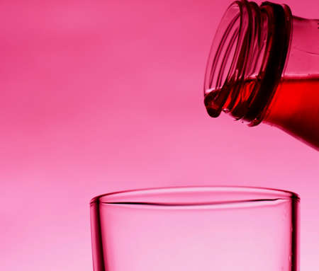 A red drink is poured into a transparent glass from a bottle. Close-up.の写真素材
