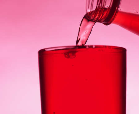 A red drink is poured into a transparent glass from a bottle. Close-up.の写真素材