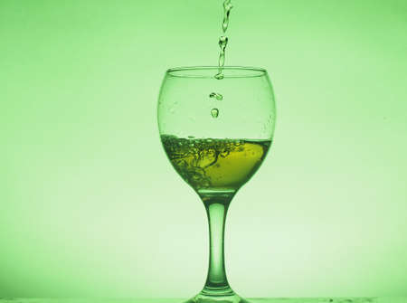 A drink (juice, cocktail, wine) is poured into a glass glass. Photo on a green background. Still-lifeの写真素材