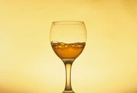 A drink (juice, wine, cocktail) is poured into a transparent glass. Photo on a yellow background. Still-life.の写真素材