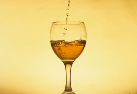 A drink (juice, wine, cocktail) is poured into a transparent glass. Photo on a yellow background. Still-life.の写真素材