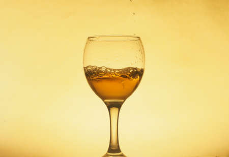 A drink (juice, wine, cocktail) is poured into a transparent glass. Photo on a yellow background. Still-life.の写真素材