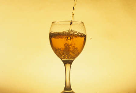 A drink (juice, wine, cocktail) is poured into a transparent glass. Photo on a yellow background. Still-life.の写真素材
